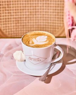 Cup of coffee with latte art served on a saucer with a spoon and a small meringue at Mademoiselle Angelina tea room.