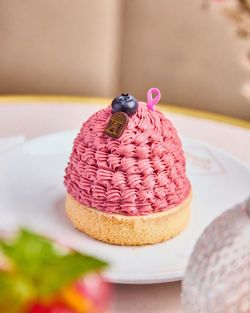 Pâtisserie Mont-Blanc au glaçage rose avec une myrtille et un petit décor en chocolat doré sur une base biscuitée.