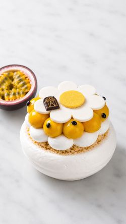 Pastry from Angelina Paris with white meringue base and yellow cream topped with a decorative flower on marble surface.