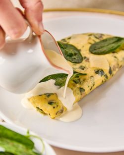 Omelette aux épinards avec sauce blanche versée dessus, servie sur une assiette blanche au salon de thé Mademoiselle Angelina