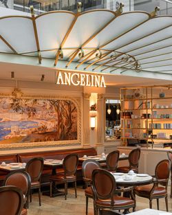 Salon de thé Angelina Paris au Château de Versailles avec tables rondes, chaises en cuir et décor classique élégant.