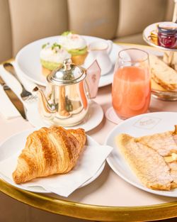A croissant, crepe, glass of juice, and silver teapot arranged on a table in a tea room at Mademoiselle Angelina.