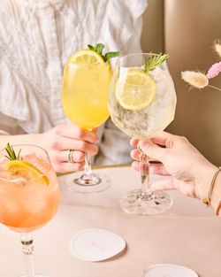 Three elegant glasses with colorful lemon-based cocktails held by two people at Mademoiselle Angelina tea room.