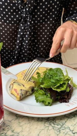 Person cutting a savory dish with sauce served with fresh greens on a white plate at Angelina Paris - Rivoli.