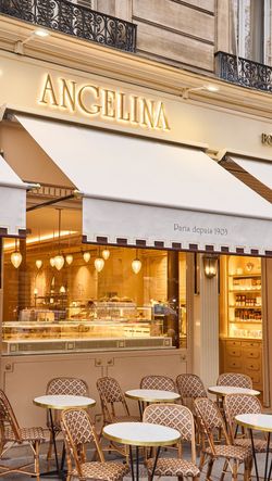Exterior view of Angelina Paris - Rivoli pastry shop with outdoor seating and illuminated sign under beige awnings.