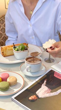 Cup of hot chocolate, salad, sandwich, macarons, and dessert with cream on a table at Angelina Paris tea room.