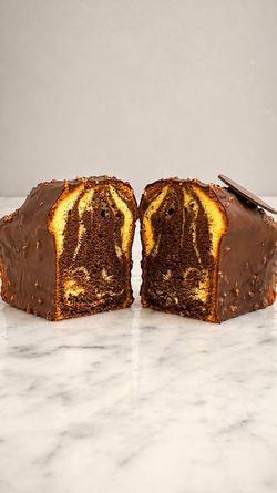 Gâteau marbré au chocolat et vanille avec glaçage au chocolat et éclats de noisettes sur un plan de travail en marbre.