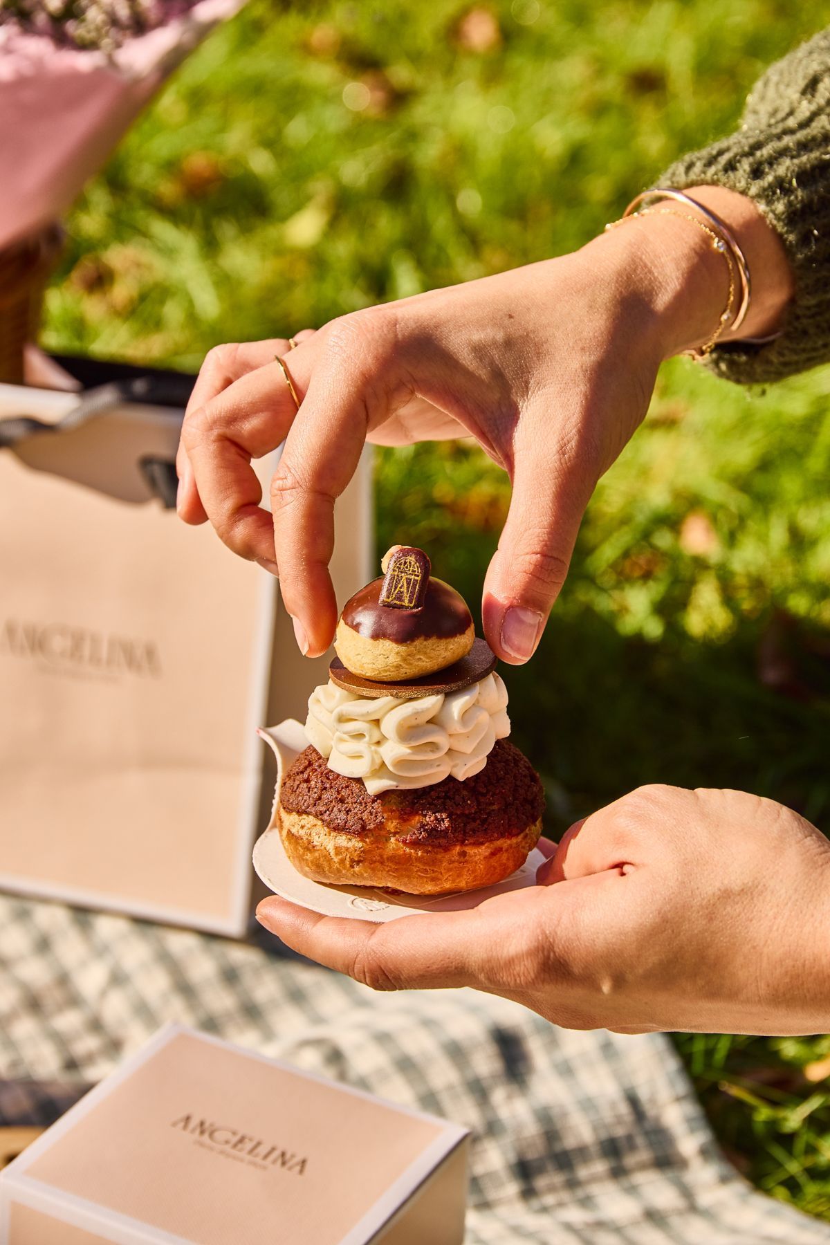 Pâtisserie élégante tenue à la main, dessert mont-blanc avec crème et chocolat, ambiance extérieure lumineuse.