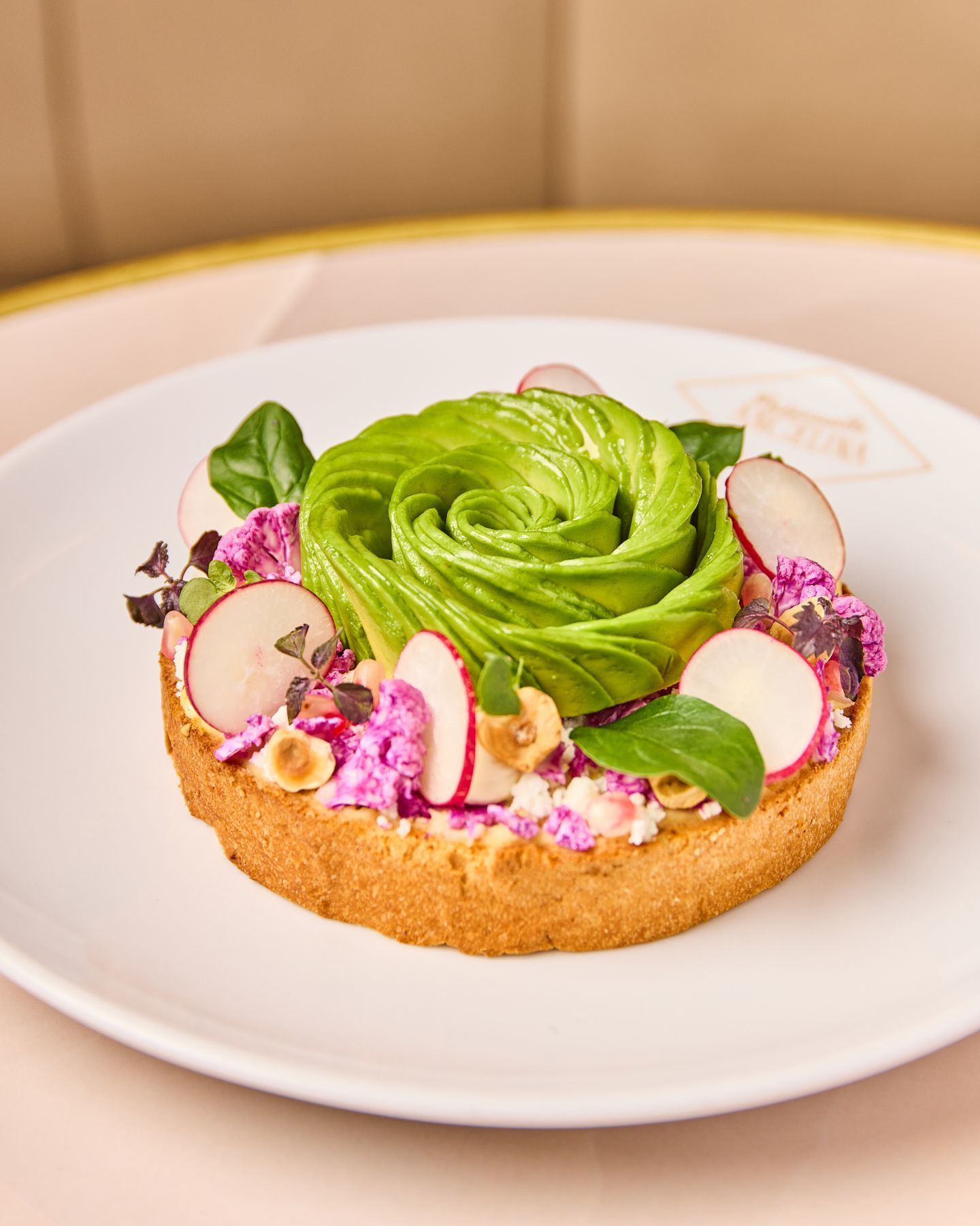 Tarte décorée d'une rose en avocat, accompagnée de radis, noisettes et fleurs comestibles dans un salon de thé.