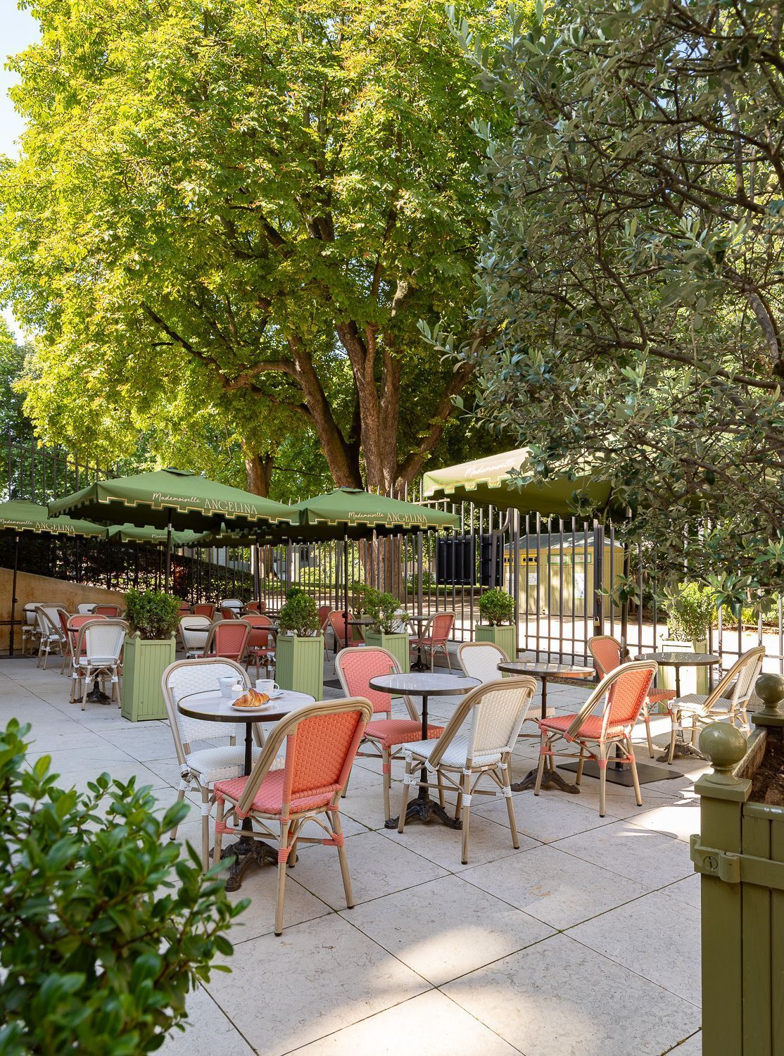 Terrasse en plein air avec tables rondes et chaises colorées sous des parasols verts entourée d'arbres feuillus.
