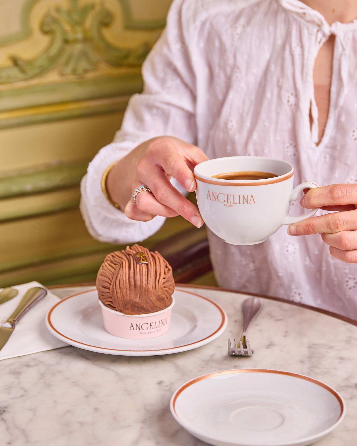 Hot chocolate and Mont-Blanc pastry served at Angelina Paris tea room with vintage decor in the background.