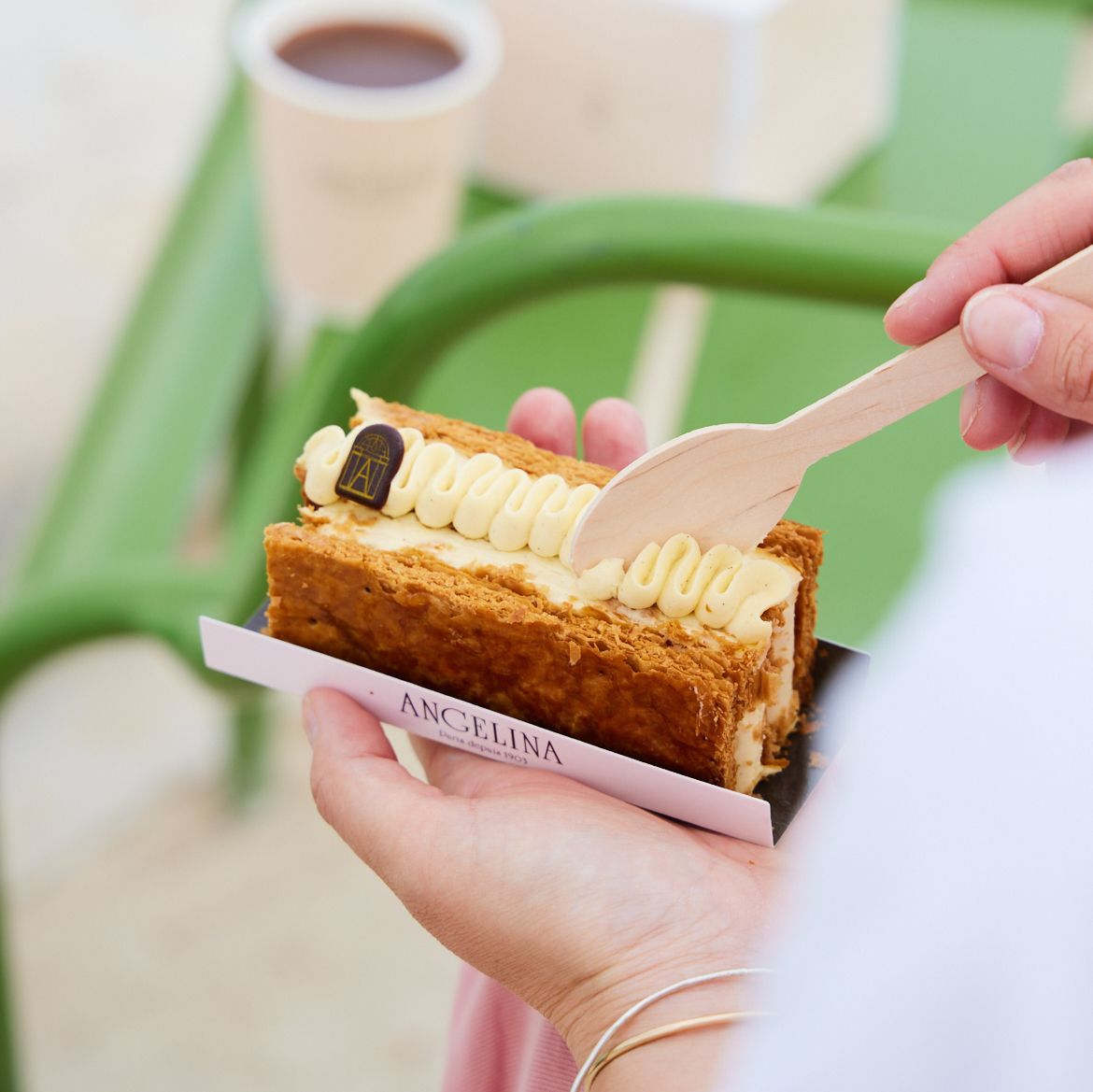 Boutique Angelina Paris pastry shop serving a custard cream mille-feuille with a cup of hot chocolate in the background.