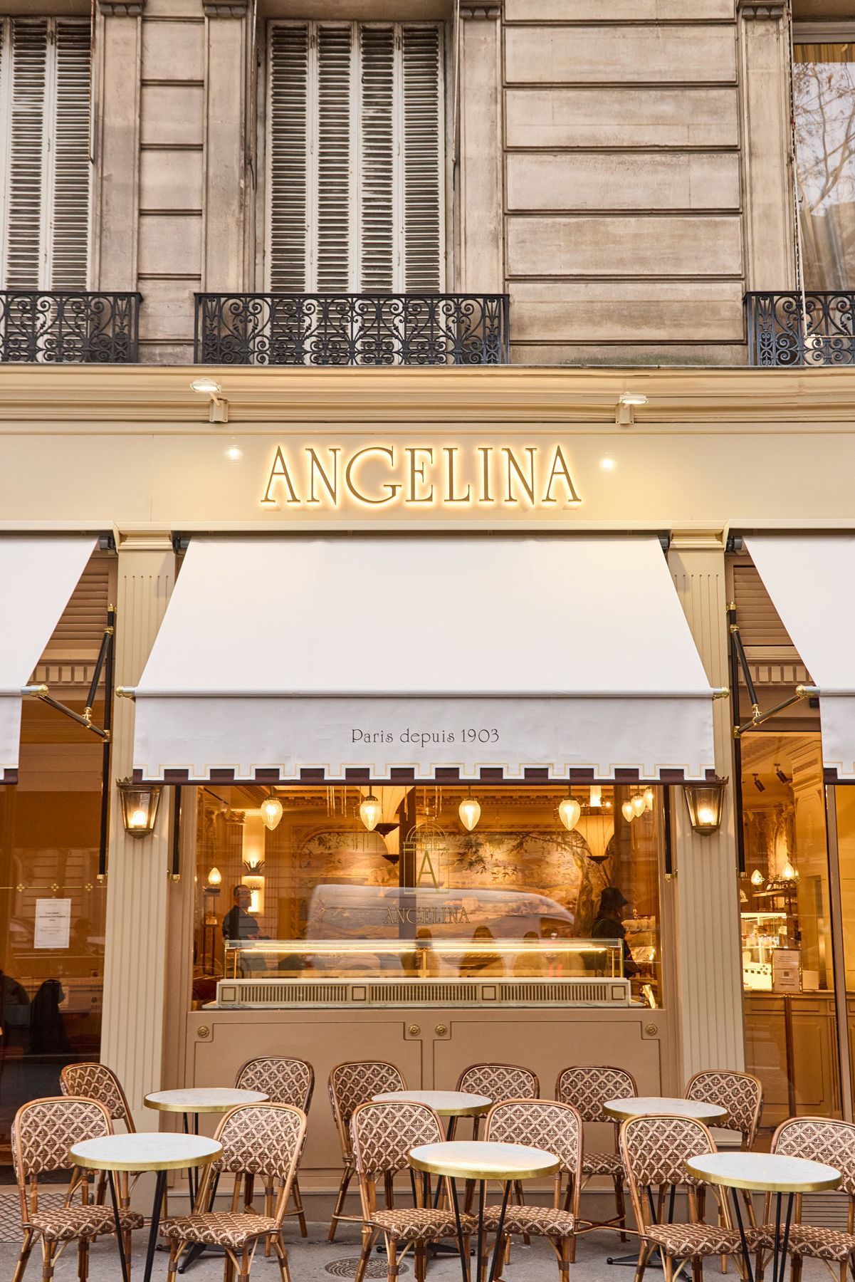 Facade of Angelina Paris – Alma tea room with outdoor seating featuring round tables and woven chairs.