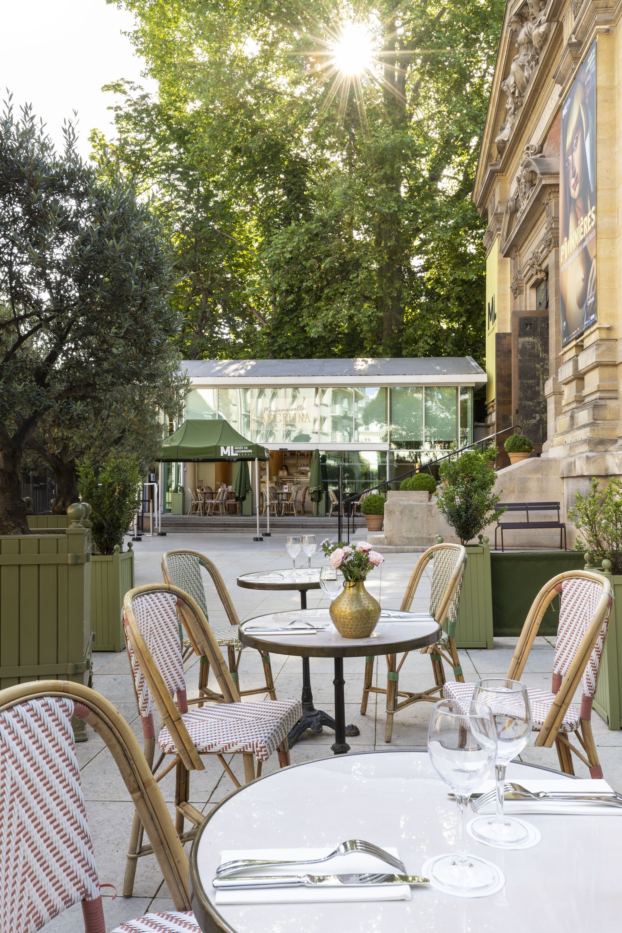 Outdoor seating area at Mademoiselle Angelina tea room with tables, chairs, and greenery under sunlight.
