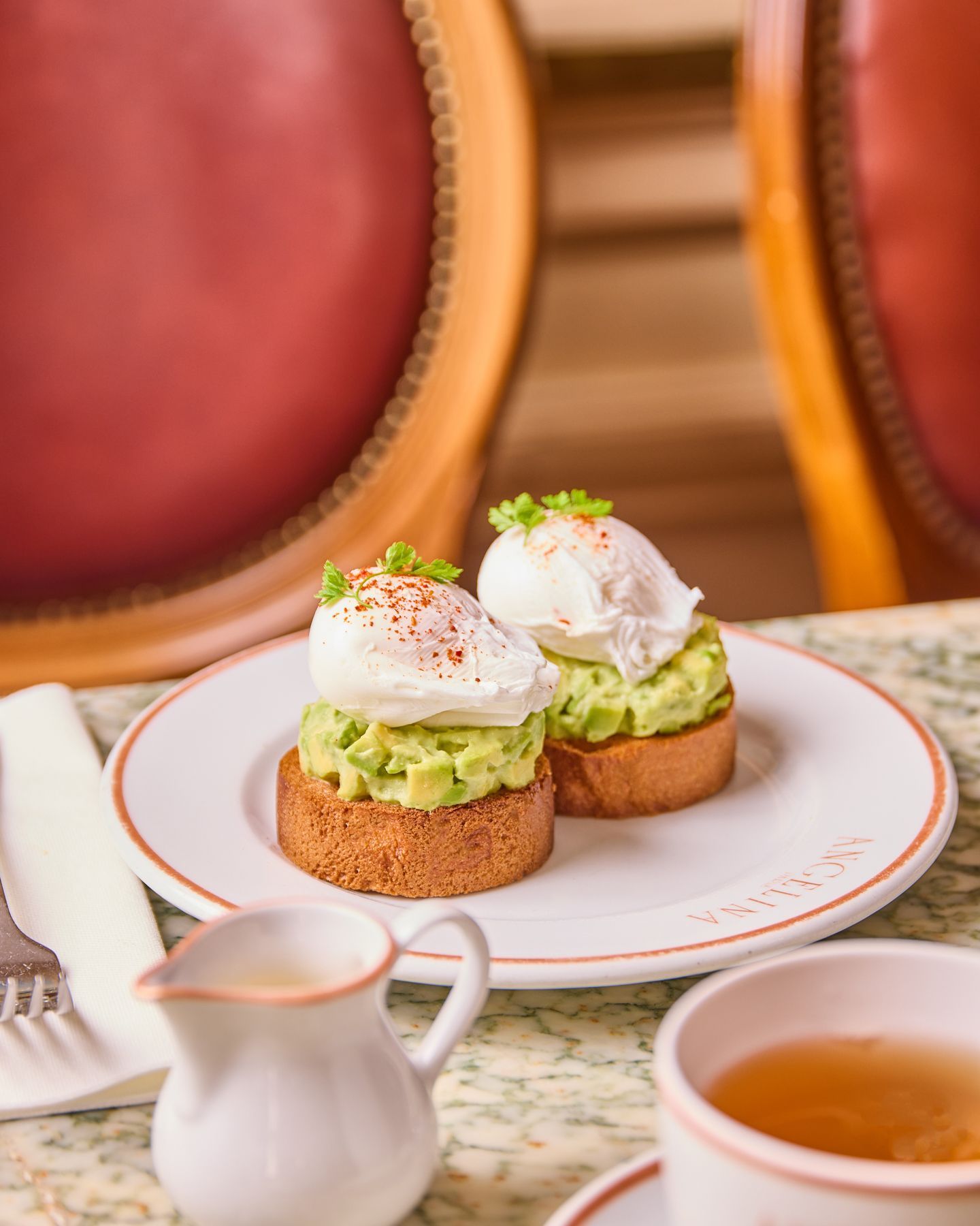 Two poached eggs on avocado toast served on a white plate at Angelina Paris - Rivoli tea room.