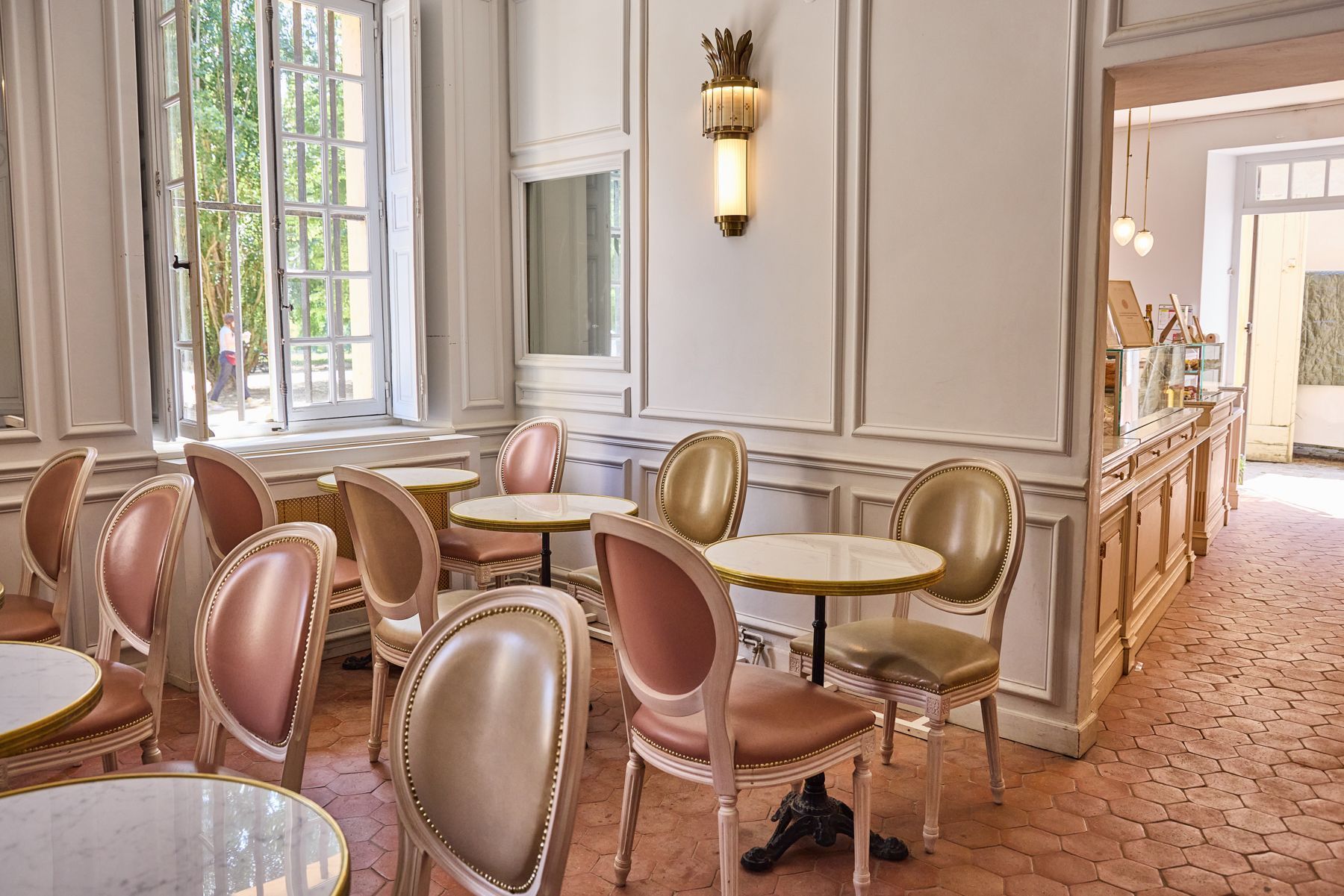 Salon de thé ancien avec chaises en cuir, tables en marbre et lumière naturelle à Angelina Paris - Domaine de Trianon.