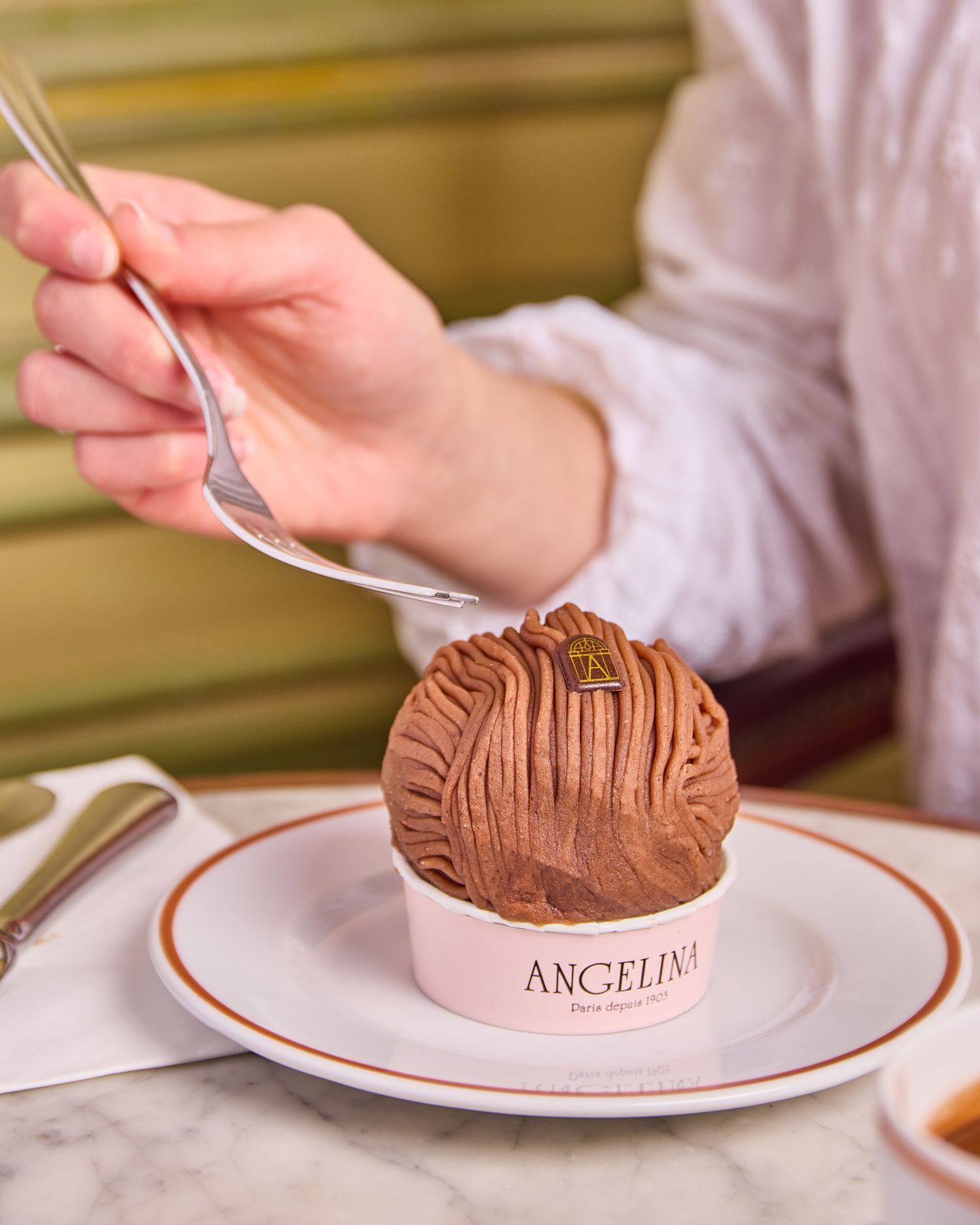 Mont-blanc au chocolat présenté sur une assiette avec un emballage portant le nom Angelina