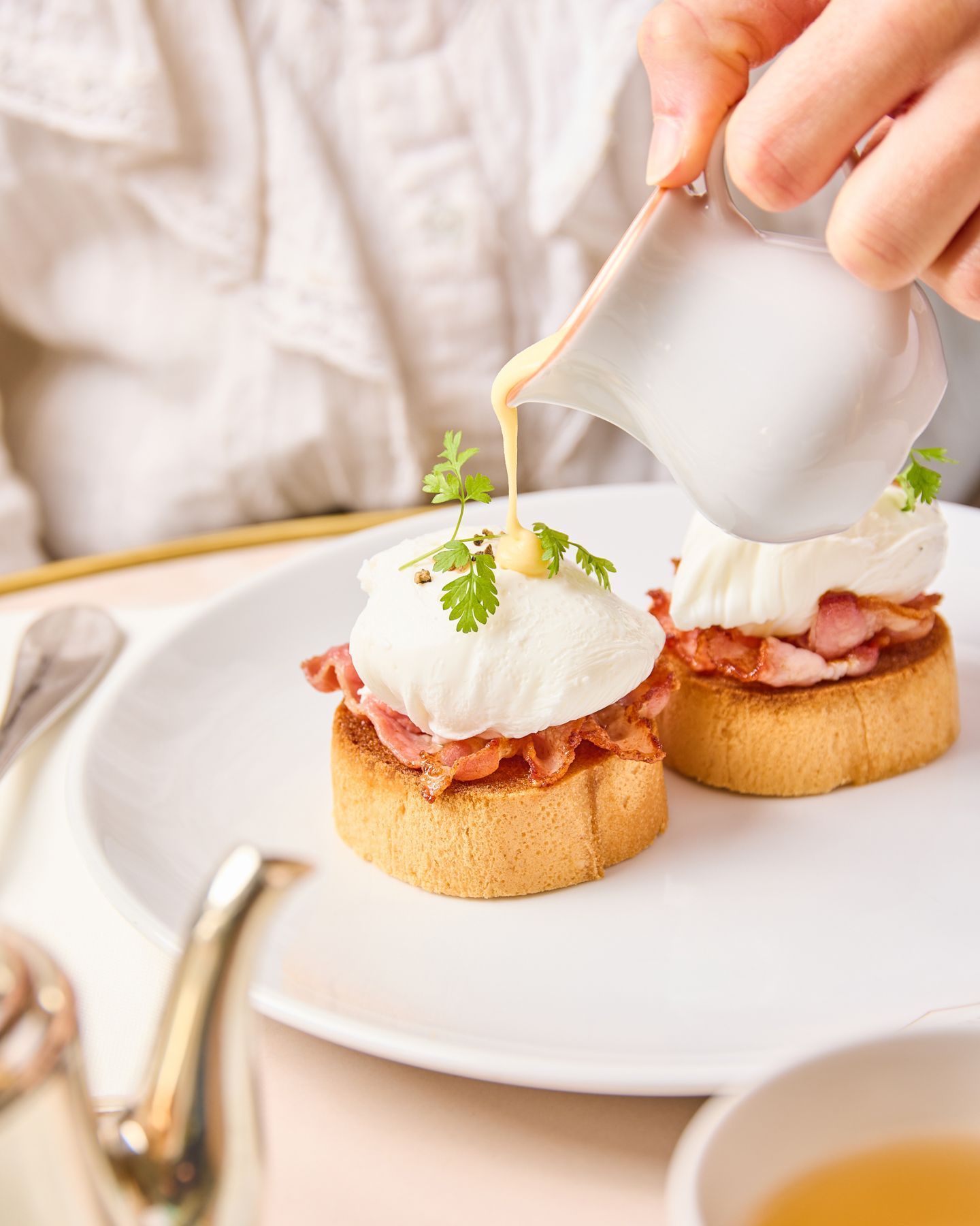 Deux toasts garnis de bacon et œufs pochés, nappés de sauce, servis dans un tea room élégant.