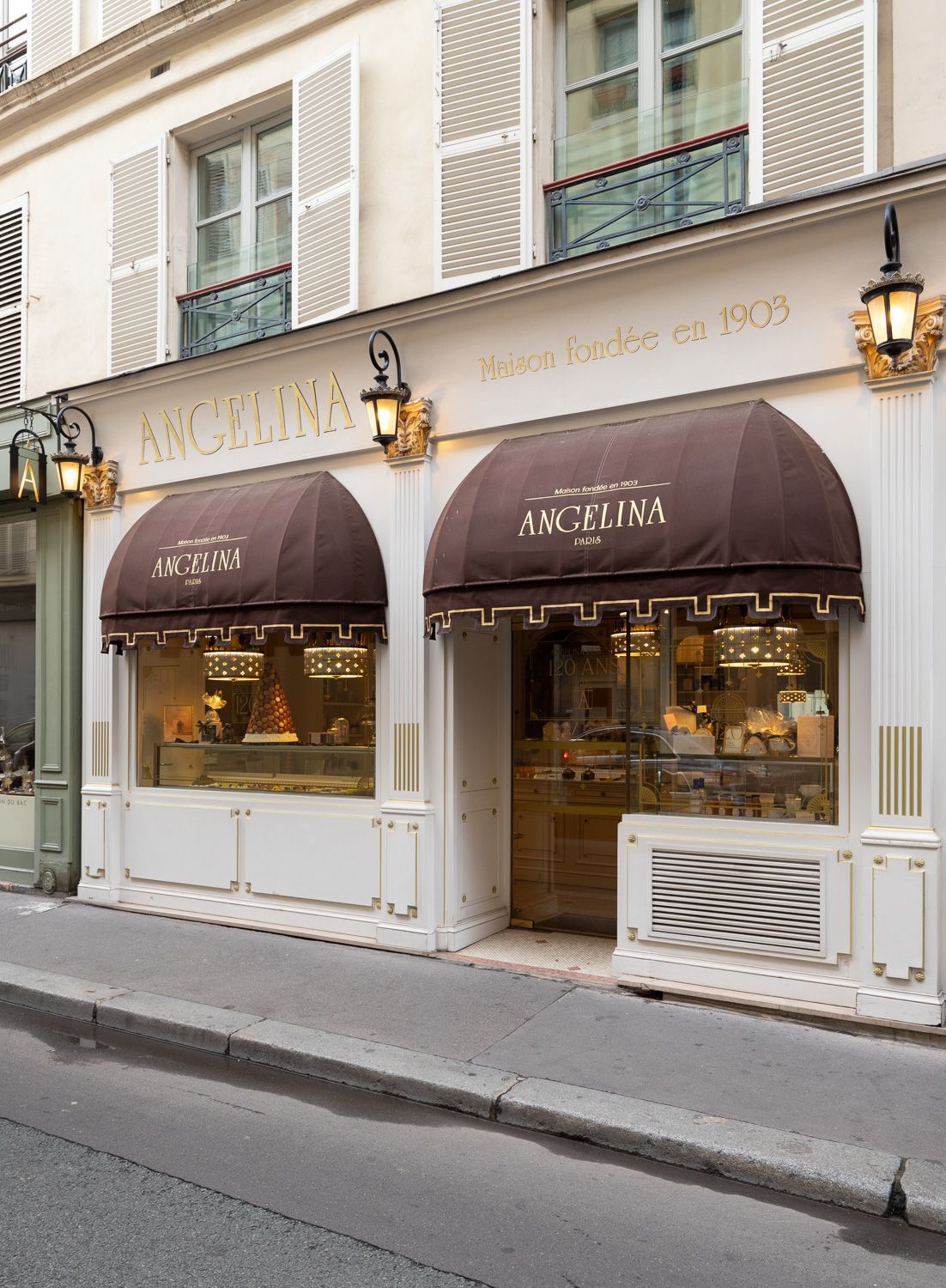 Façade de la pâtisserie Boutique Angelina Paris avec ses stores bruns et ses lanternes extérieures.