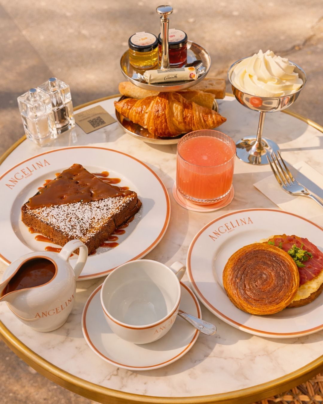Croissant, chocolate cake, pastry with cream, and pink juice served on Angelina Paris tea room table.