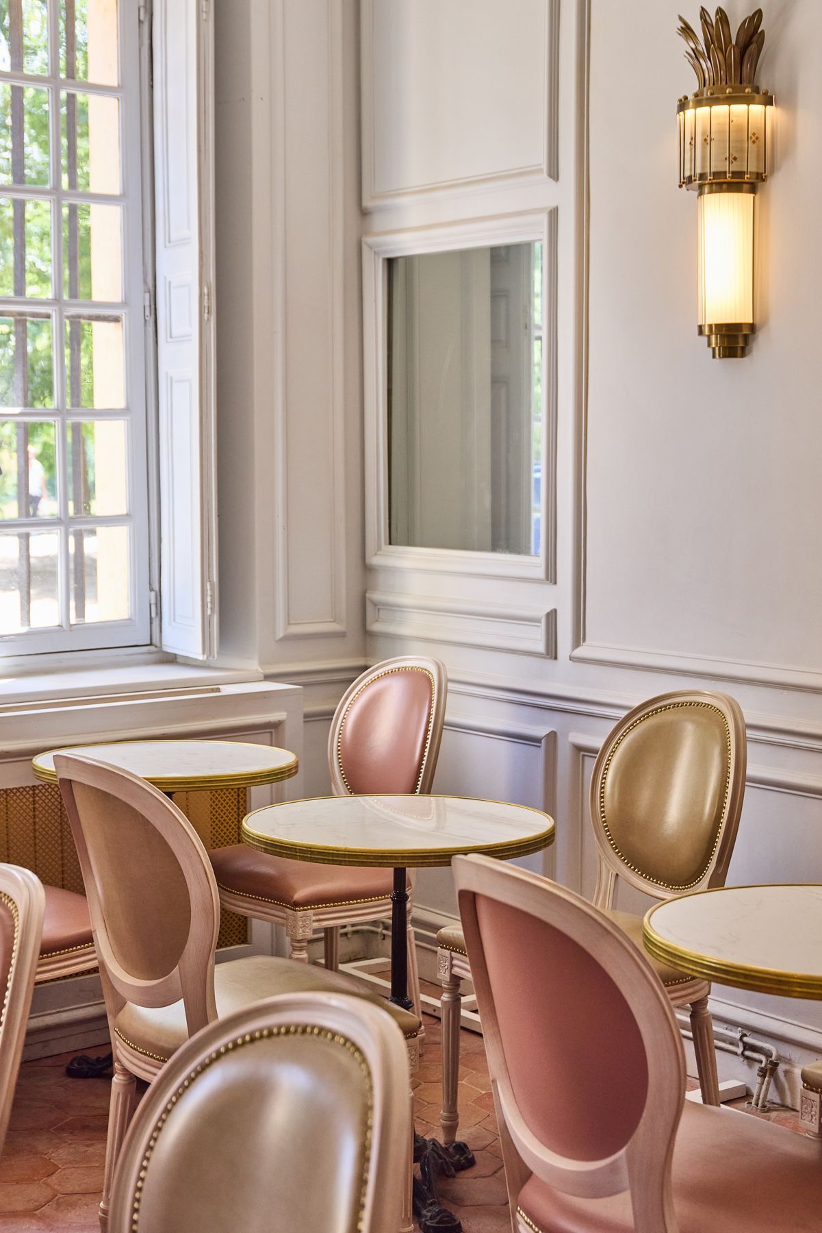 Tea room seating with round marble tables and elegant pink and beige chairs at Angelina Paris - Domaine de Trianon.