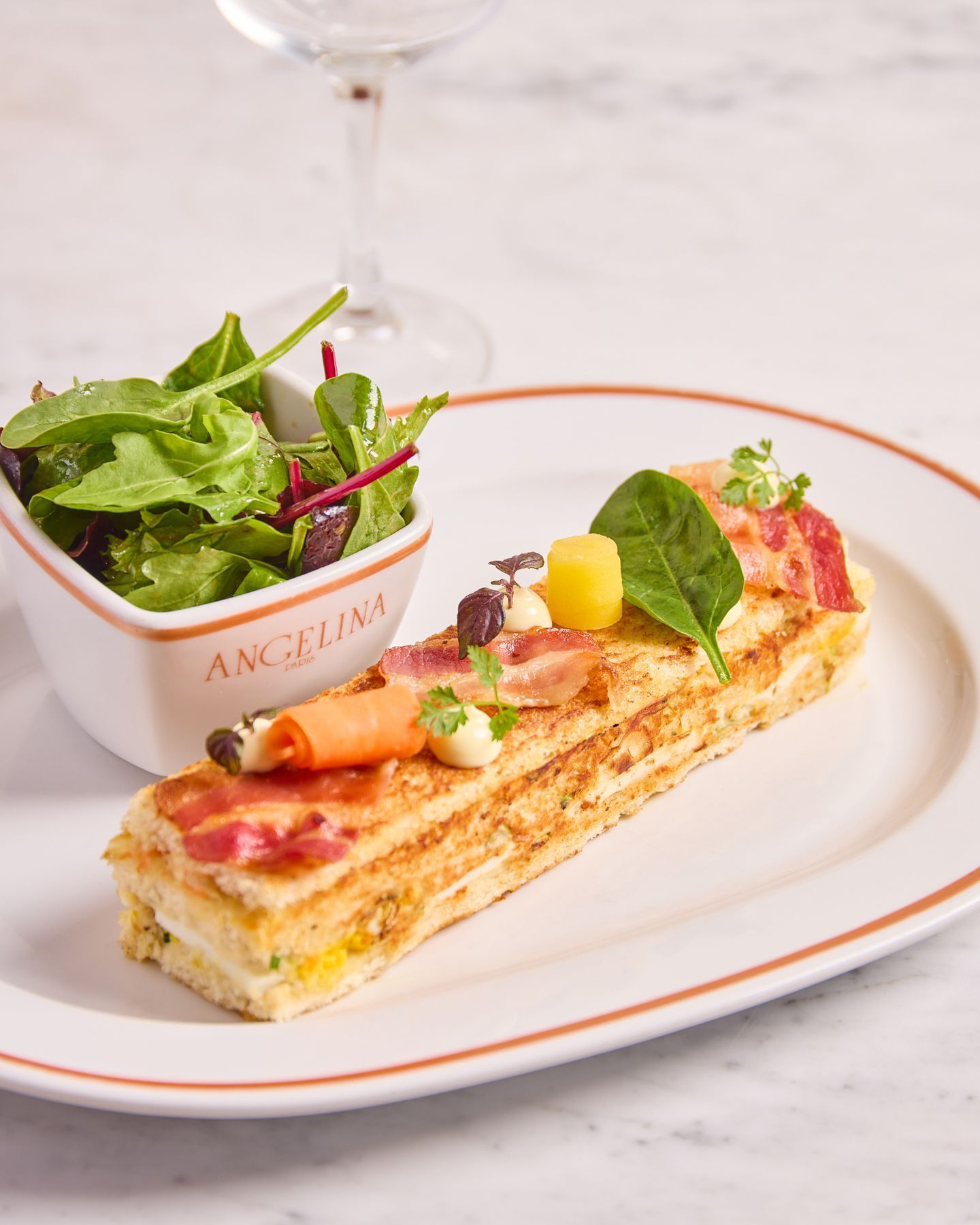Gourmet layered savory dish with bacon and vegetable garnishes served with a fresh green salad at Angelina Paris.