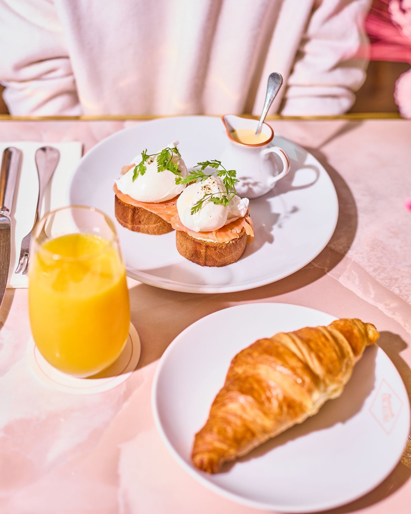 Two slices of bread with poached eggs and herbs, a croissant on a plate, and a glass of orange juice on the table.
