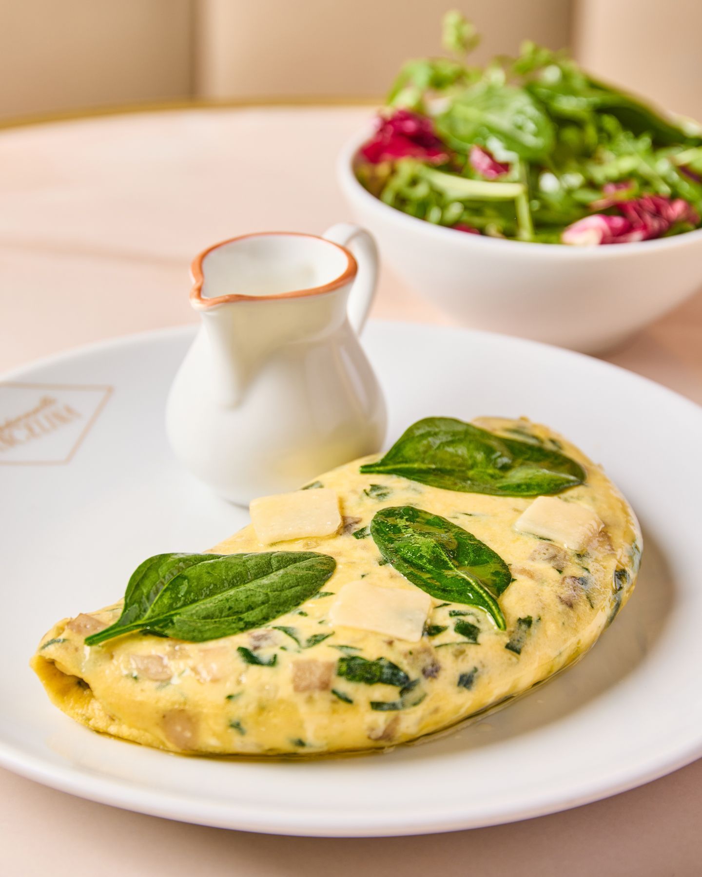 Omelette aux épinards et fromage servie avec une petite carafe de sauce, accompagnée d'une salade verte en arrière-plan.