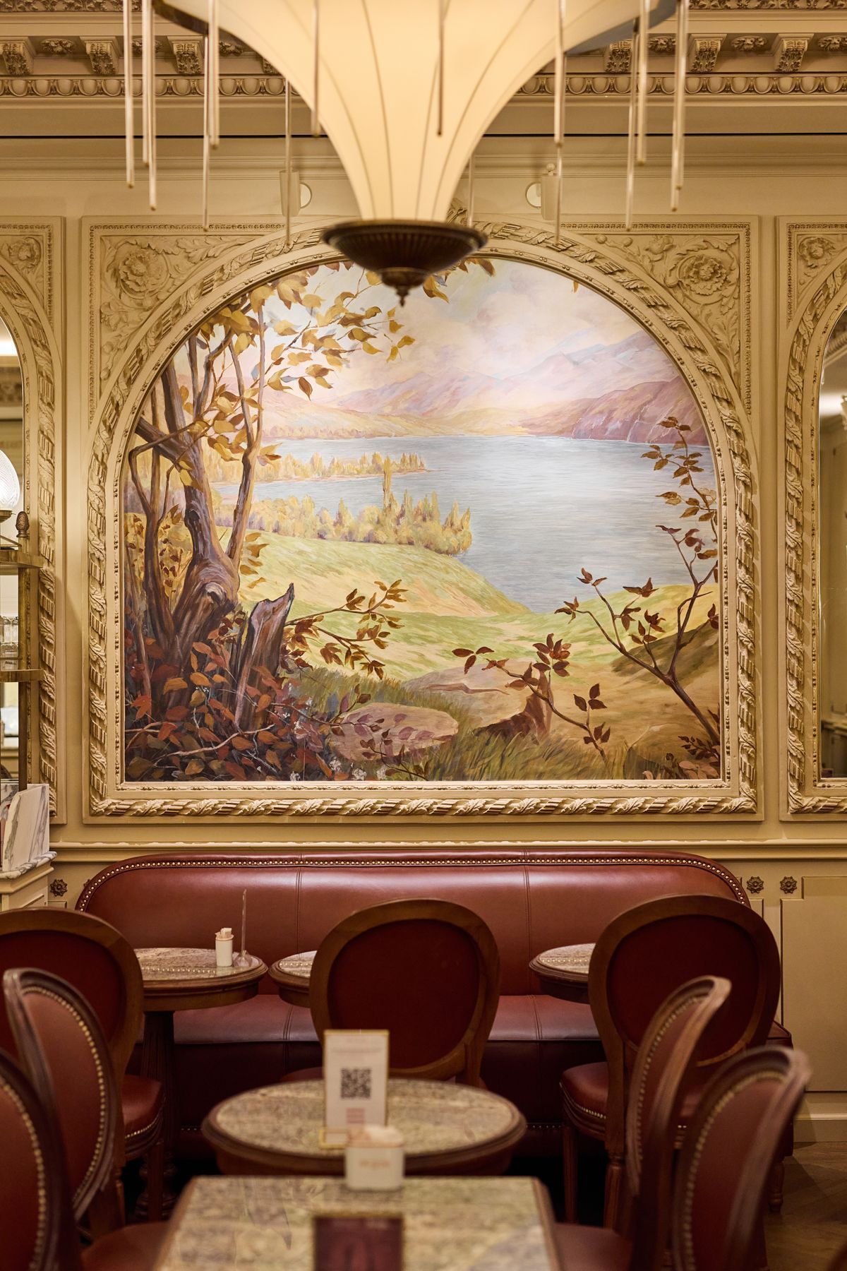 Interior of Angelina Paris tea room with red leather chairs and landscape painting on the wall.