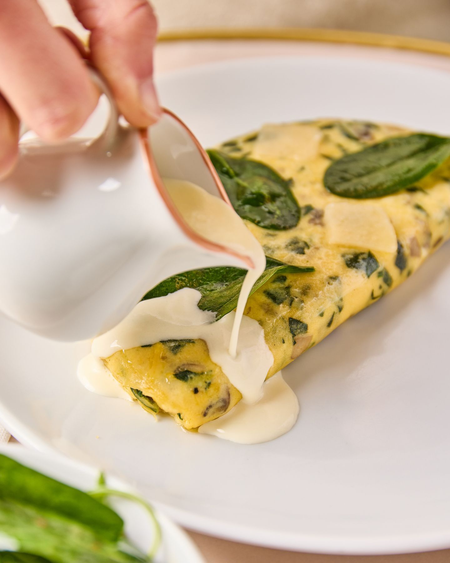 Creamy white sauce being poured on a spinach omelette on a white plate at the tea room.