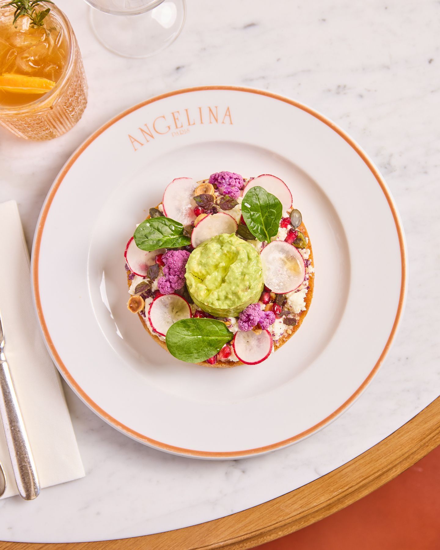 Assiette blanche Angelina avec une tartine garnie d'avocat, radis, chou-fleur violet et jeunes pousses sur une table ronde.