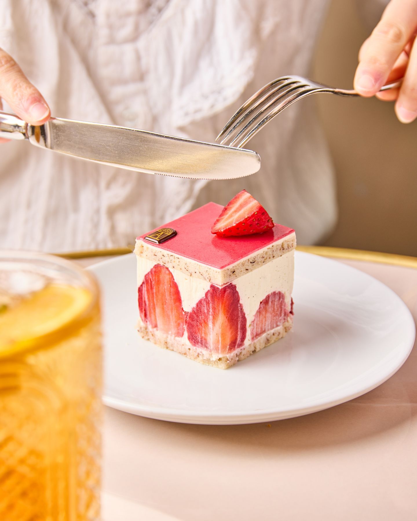 Pâtisserie cubique garnie de fraises tranchées et d'une fine couche de glaçage rouge, servie sur assiette blanche.