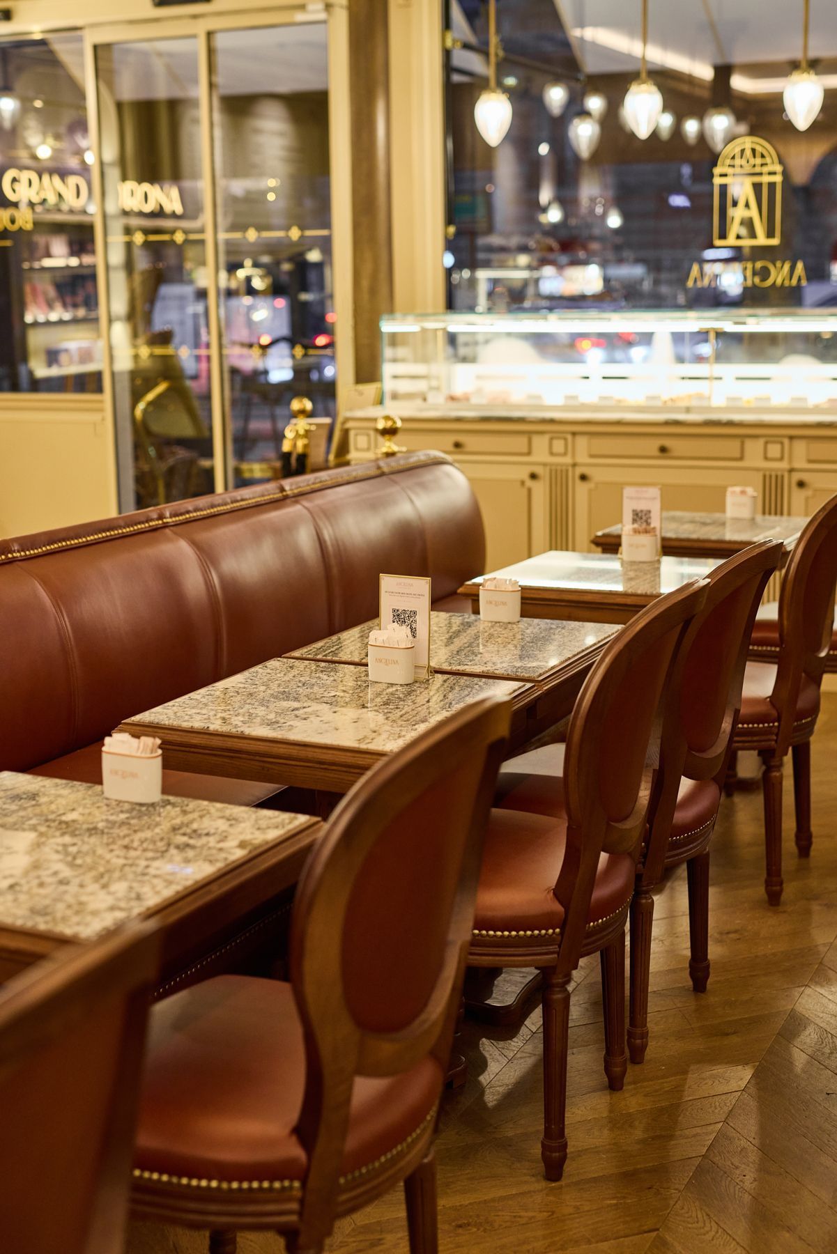 Cozy interior of Angelina Paris tea room with marble tables, brown leather seating, wooden chairs, and warm lighting.