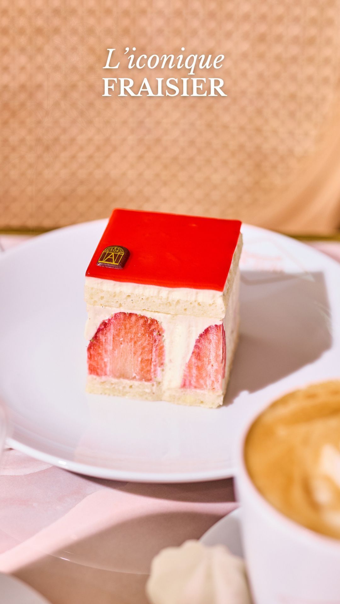 Strawberry fraiser cake slice on a white plate with a cup of coffee in the foreground at the tea room.