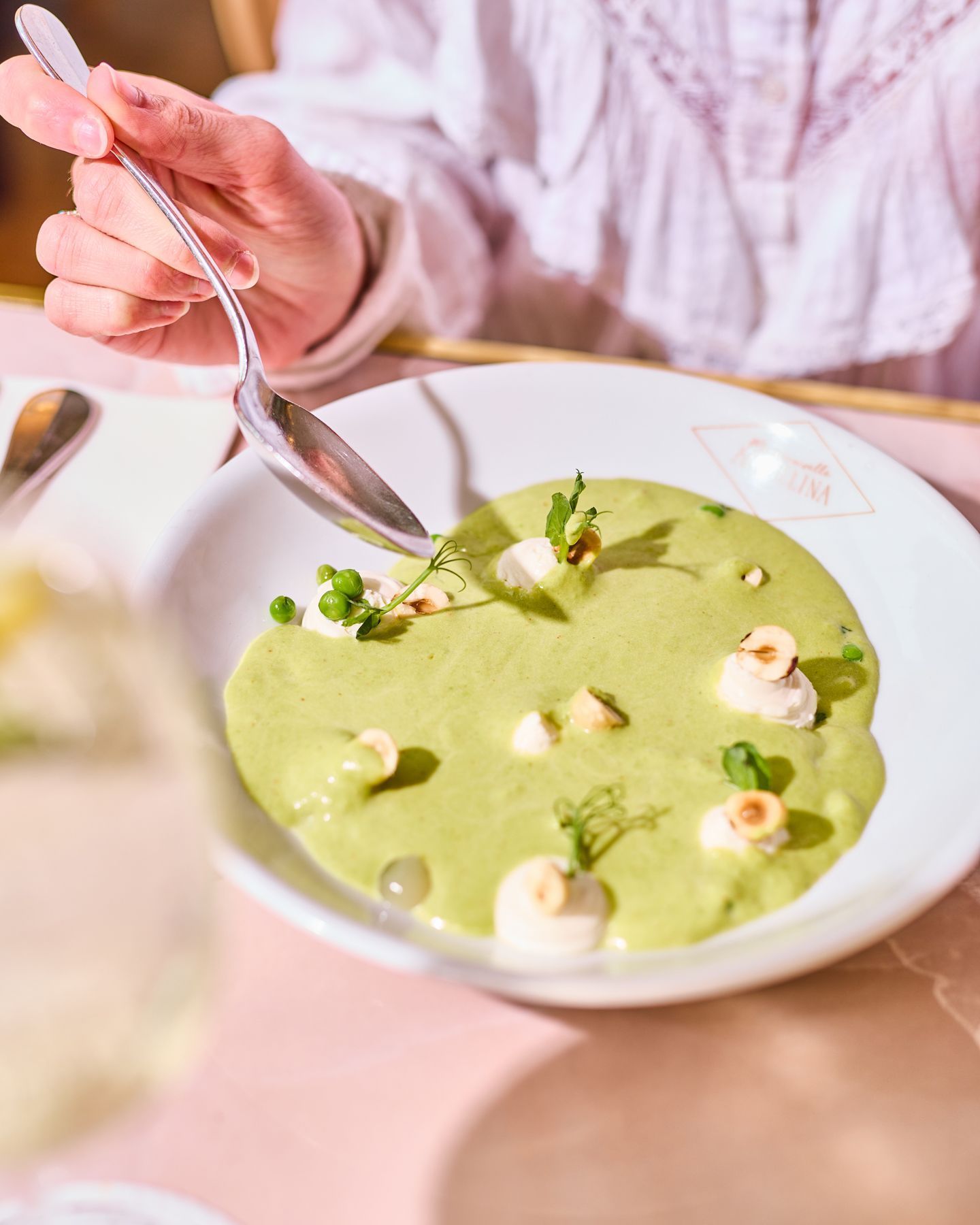Green pea soup garnished with herbs and small white elements, served in a white bowl at a tea room.