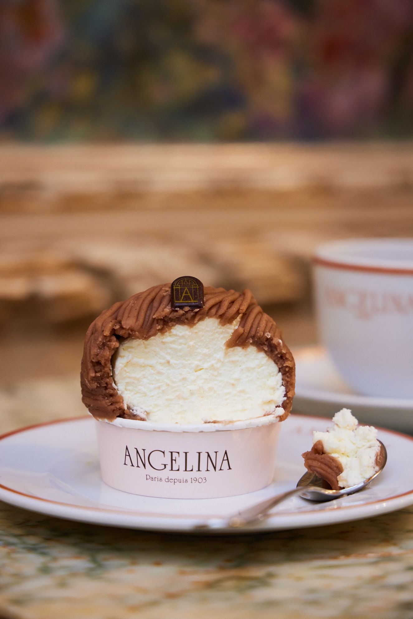 Mont-blanc classique servi dans un pot avec le logo Angelina, présenté sur une assiette avec une cuillère.