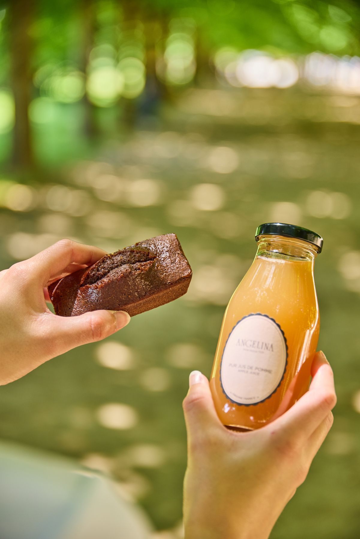 Petit gâteau au chocolat et bouteille de jus d'orange tenus à la main dans un cadre extérieur lumineux et verdoyant