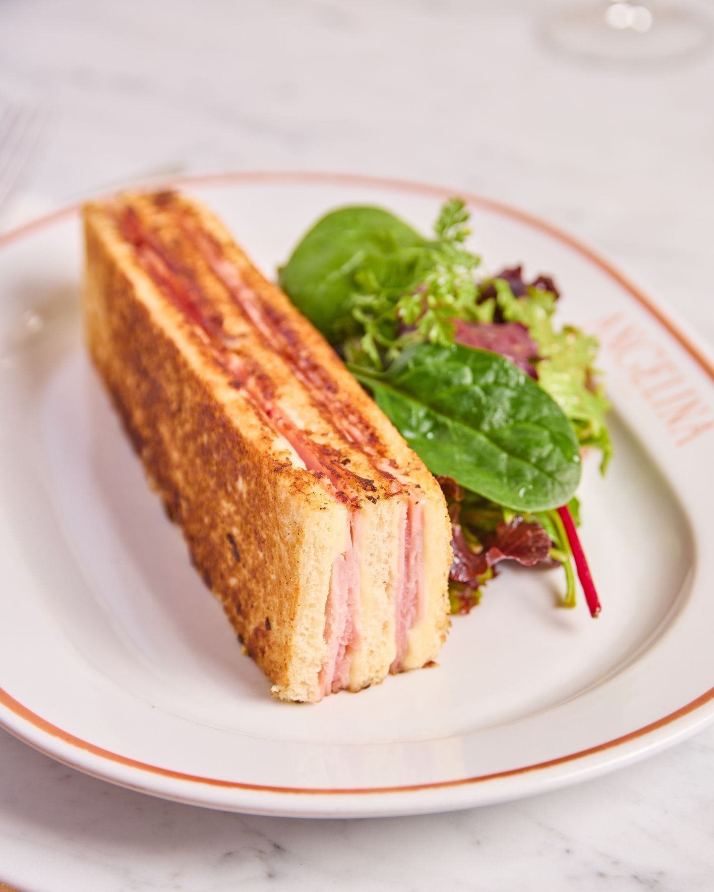 Croque-monsieur accompagné d'une salade verte sur une assiette de la pâtisserie Angelina Paris à Versailles.