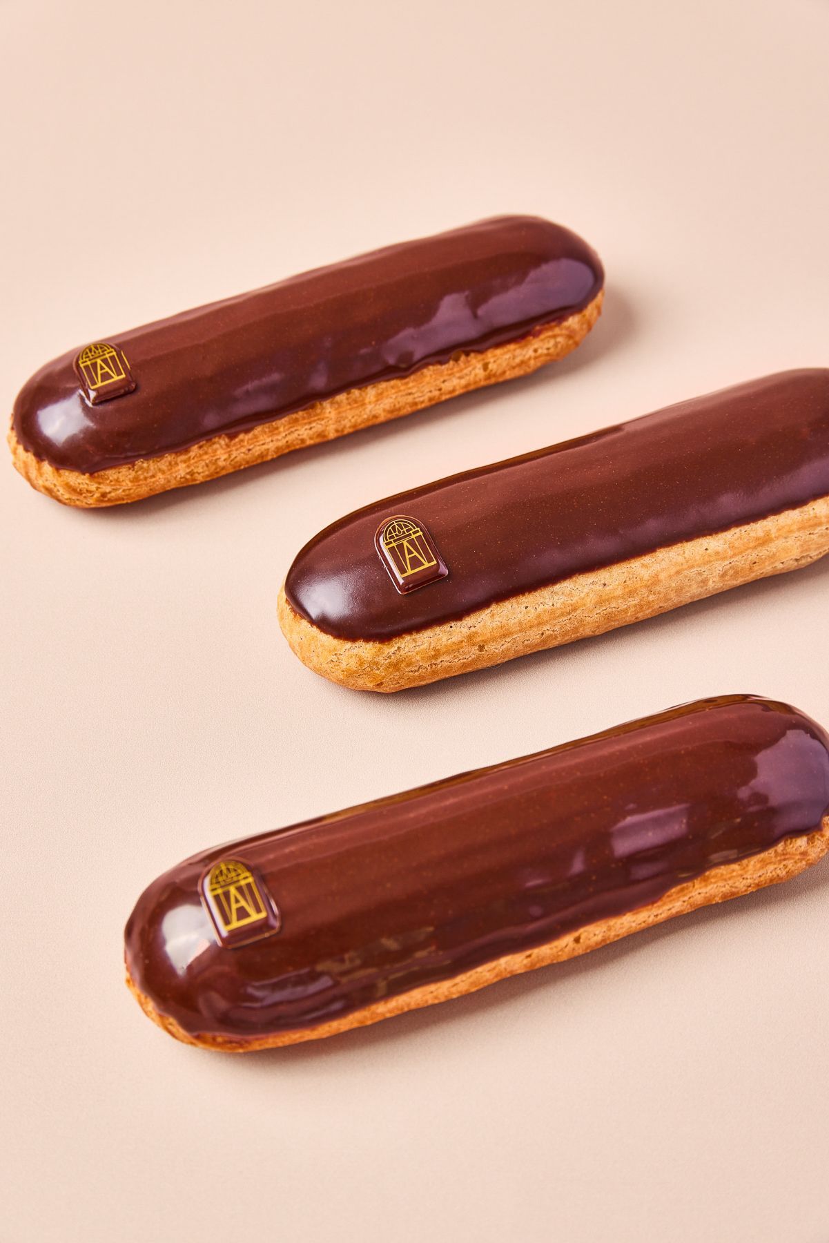 Éclairs au chocolat brillant avec un glaçage lisse, ornés d'une petite plaque décorative Boutique Angelina Paris.